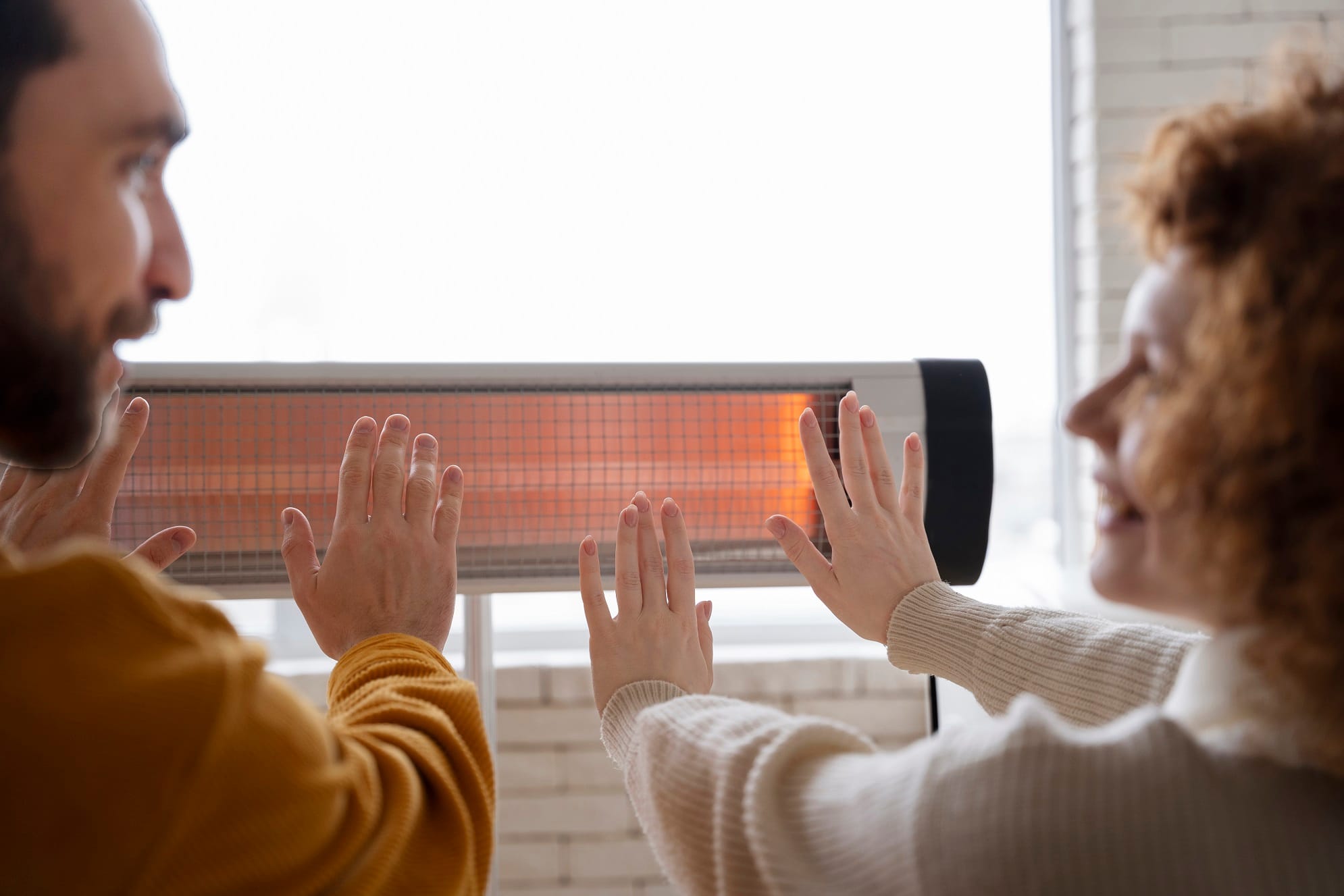 smiley-couple-warming-up-hands-near-heater